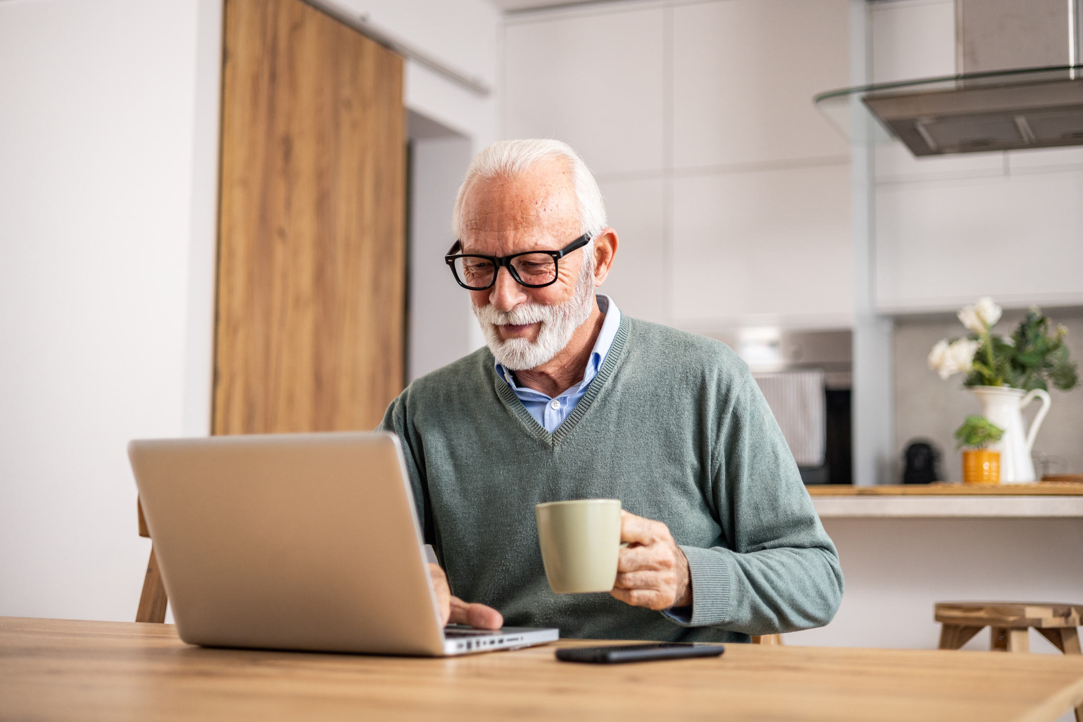 Older man using a laptop at his kitchen table.