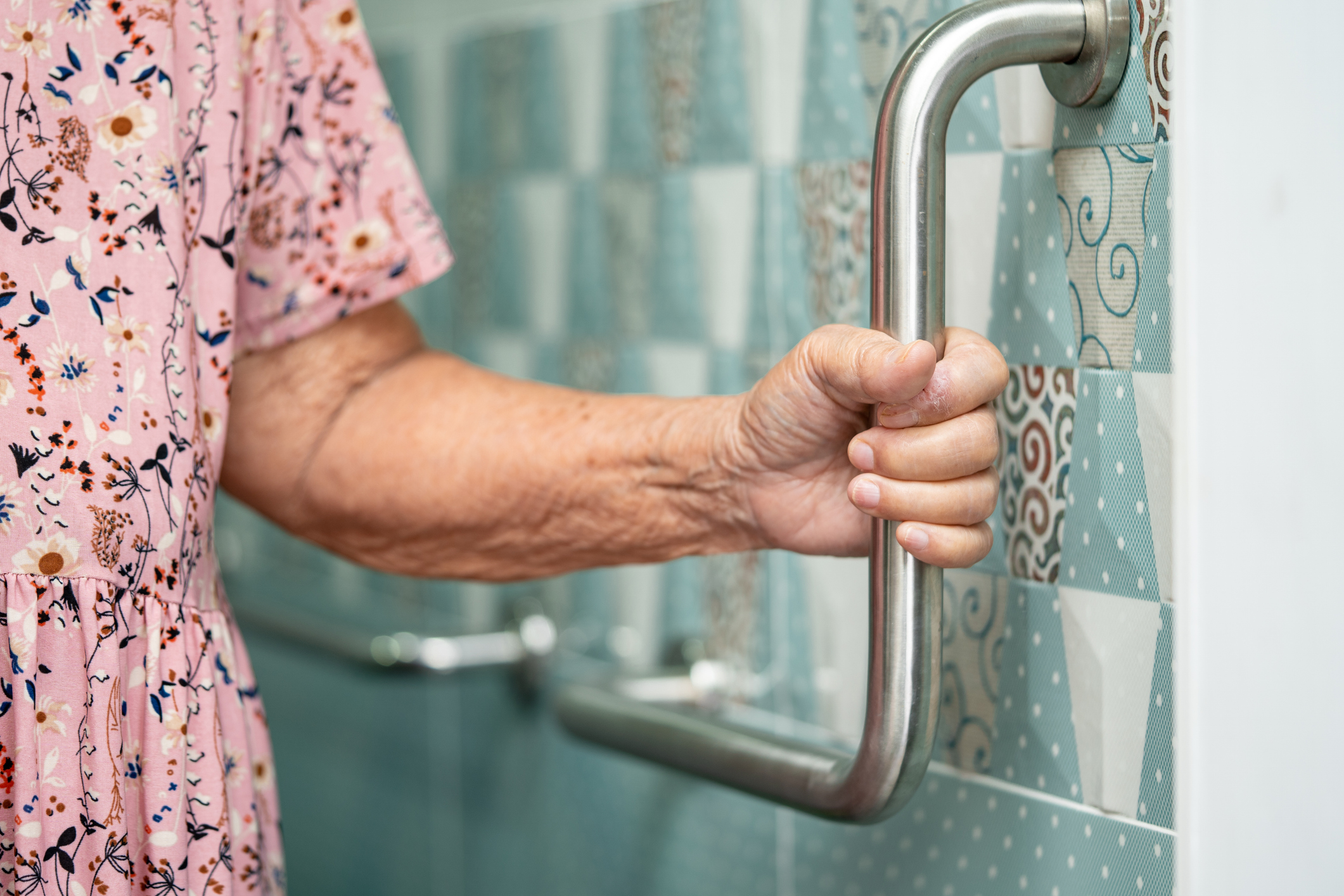 A hand holding a grab bar in a bathroom.