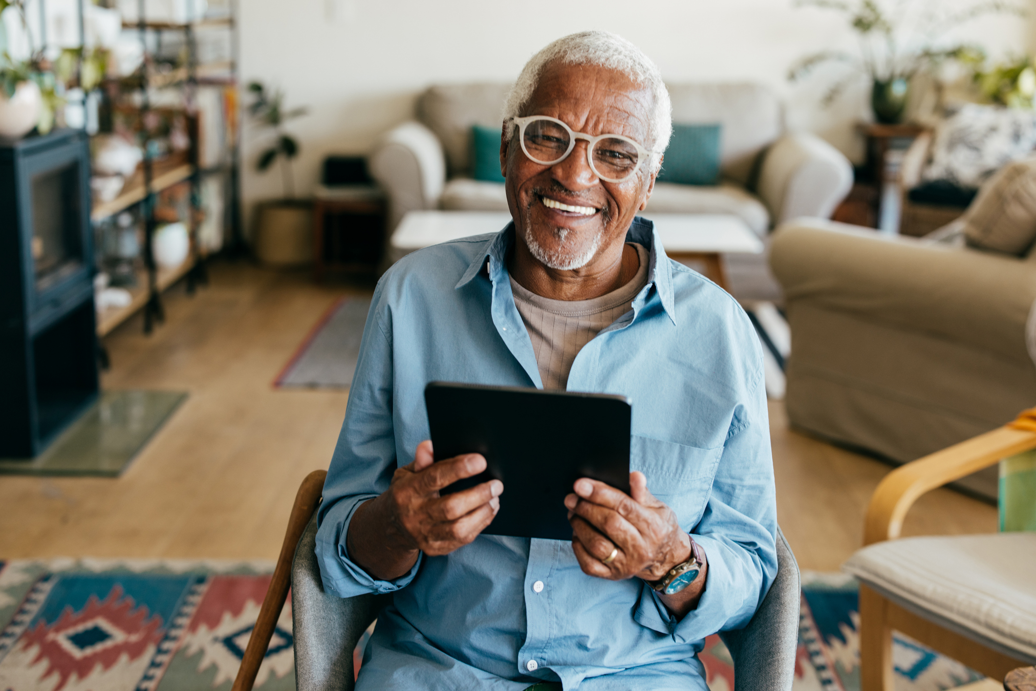Smiling older man holding a tablet in his living room.